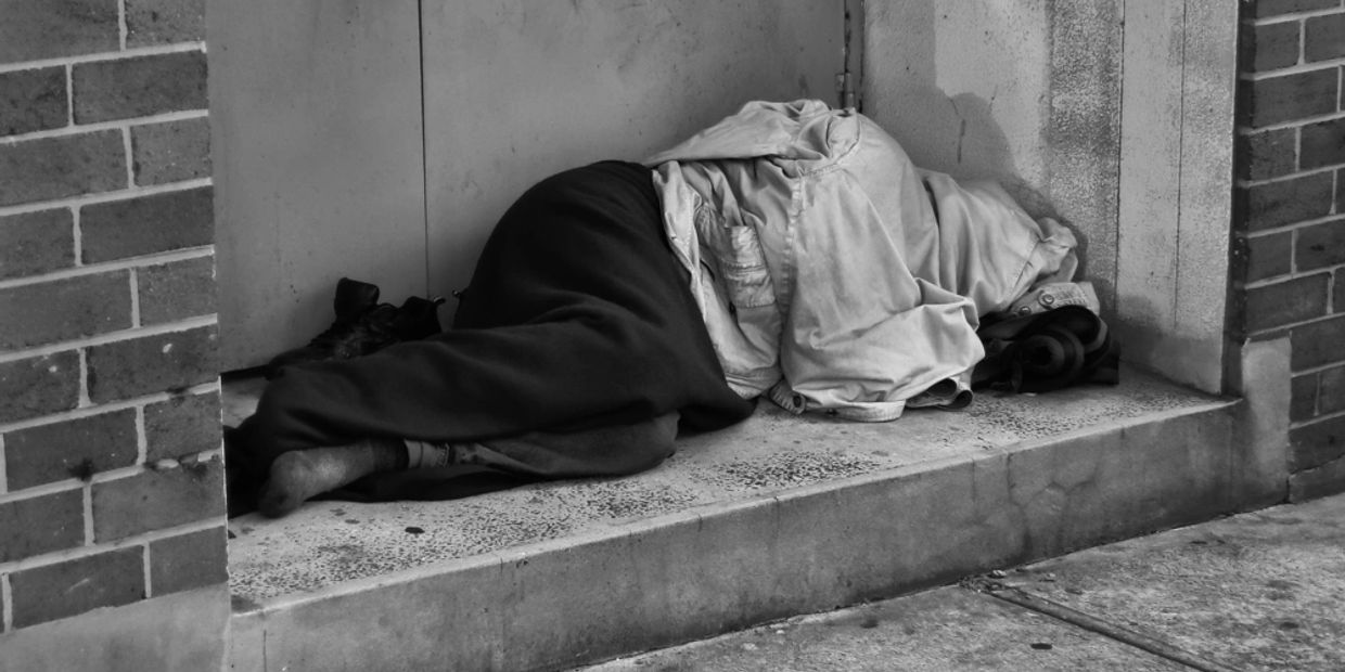 A person sleeping on a concrete step, covered in a jacket, black and white photo.