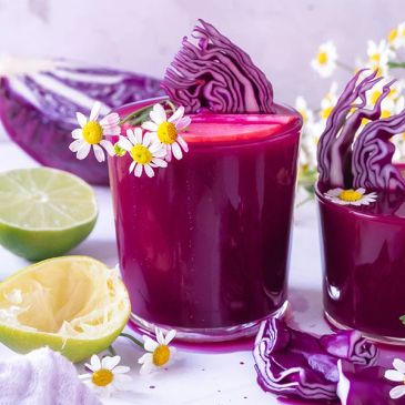 Vibrant purple cabbage juice served with lime and decorated with chamomile flowers.