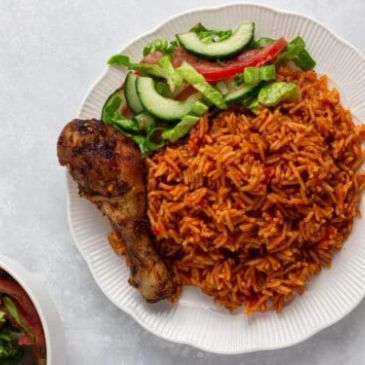 Plate with jollof rice, grilled chicken drumstick, and fresh salad.