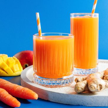 Two glasses of fresh orange juice with carrots, mango, and ginger.