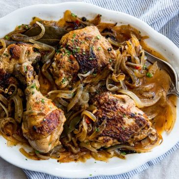 Roasted chicken thighs with caramelized onions and herbs on a white platter.