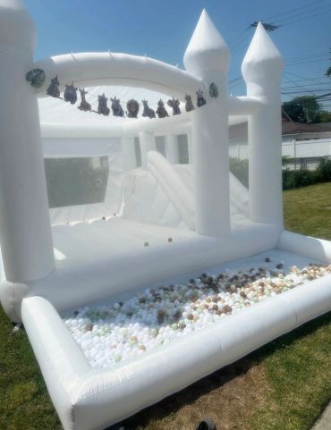 White inflatable bounce house with animal decorations and ball pit outside.