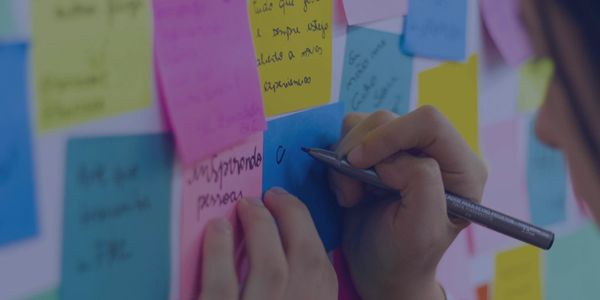Woman writing on a sticky note amid many multicolored notes. | Photo by Bruno Bueno from Pexels