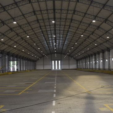 Spacious, empty warehouse with high arched ceiling and marked parking spots.
