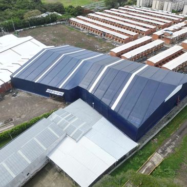 Aerial view of large industrial warehouse with blue roof and surrounding buildings.
