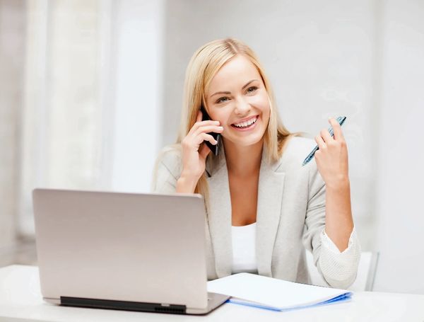 Happy woman talking on phone at laptop.