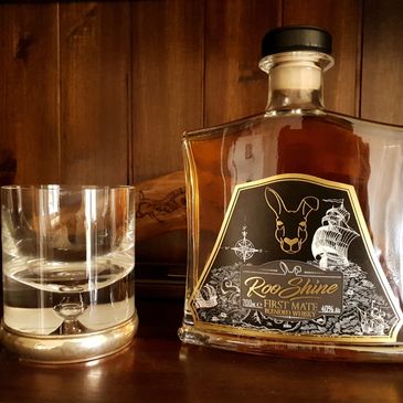 A bottle of Roo Shine whiskey and an empty glass on a wooden surface.