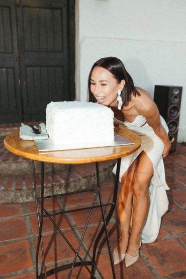 bride who had her professional makeup done standing infront of a wedding cake looking happy. 