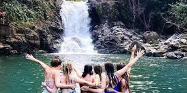 Group of friends enjoying a waterfall and lake together, arms around each other.
