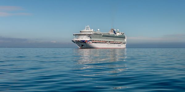 A large cruise ship sailing calmly on a clear blue sea under a clear sky.