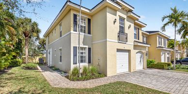 Two-story beige townhouse with garage and palm trees.
