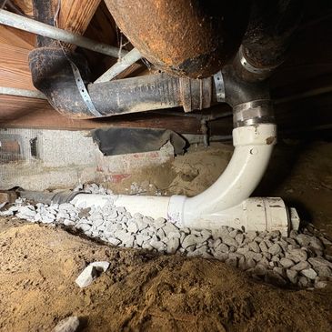 New sewer pipe and fittings installed under a house crawl space with gravel base replacing a deteriorated section of cast iron.