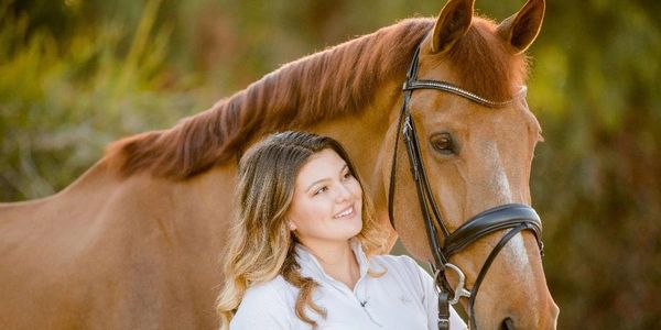 A woman smiling affectionately at a brown horse outdoors.