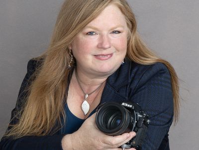A smiling woman holding a Nikon camera.