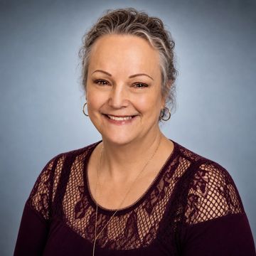 Smiling middle-aged woman with curly gray hair and lace top.