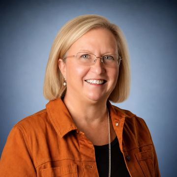Smiling woman with blonde hair wearing glasses and an orange jacket.