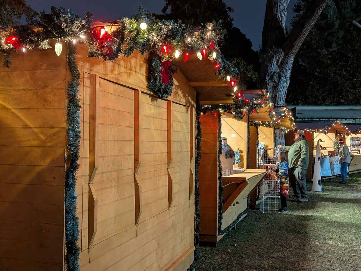 Holiday market stalls decorated with festive lights at night.