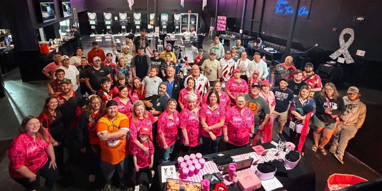 Large group of people gathered indoors, many wearing pink shirts and posing for a photo.