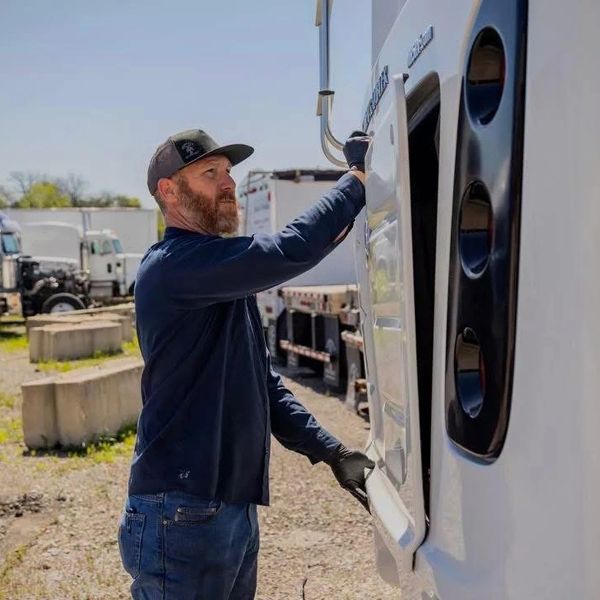 Man inspecting or working on a white truck outdoors.
