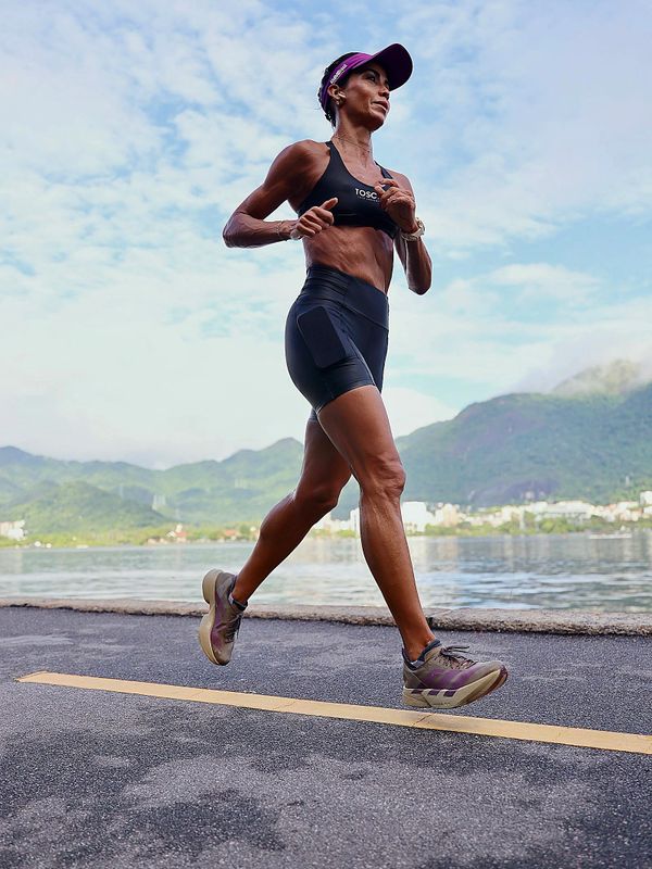 Athletic woman running outdoors along a waterfront with mountains in the background.