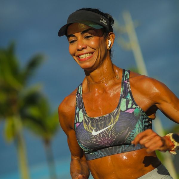 Smiling woman running outdoors wearing sportswear and a visor.