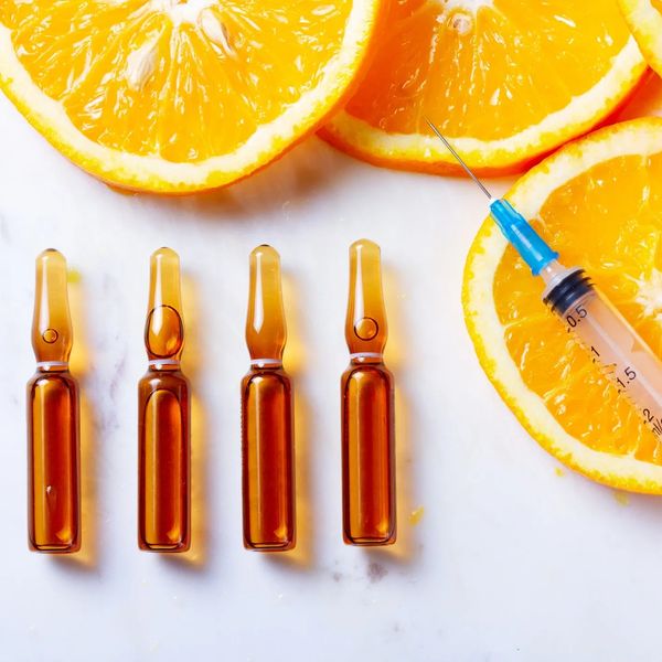 Vitamin C ampoules and a syringe next to sliced oranges.