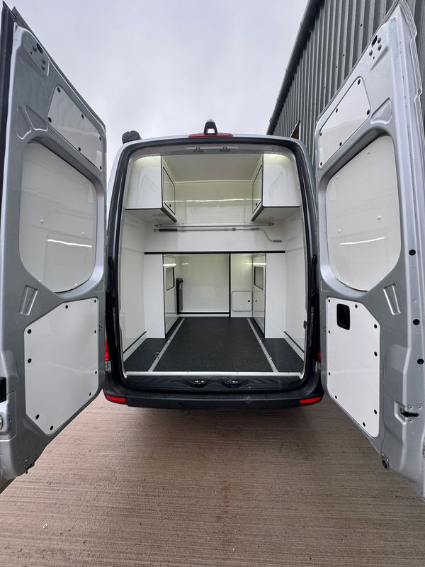Empty cargo van with open rear doors and built-in storage compartments.