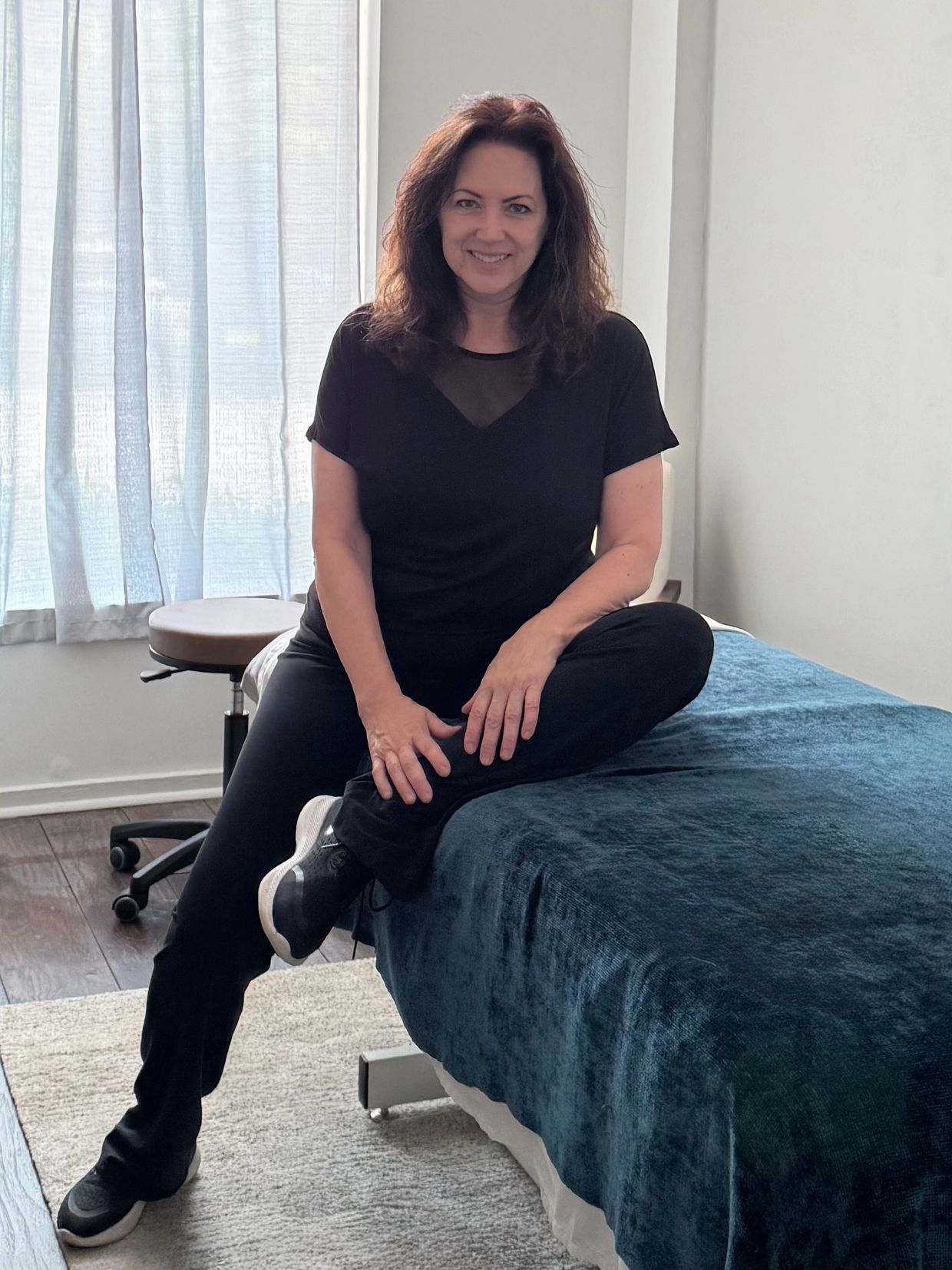 Woman sitting on the edge of a massage table in a casual outfit.
