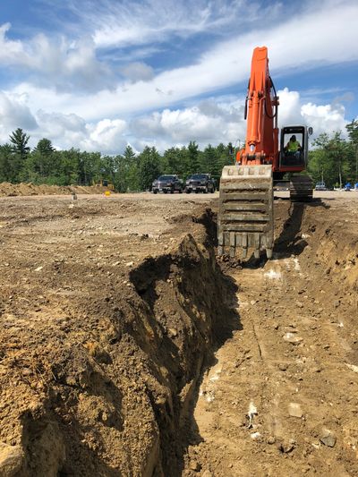 Excavator digging a trench on a construction site under blue sky.