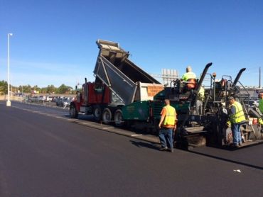Workers paving a road with machinery under a clear sky.
