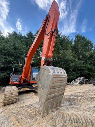 Orange excavator with large bucket on dirt ground.