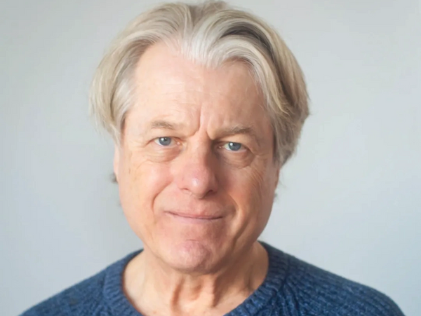 Portrait of a smiling older man with gray hair in a blue sweater.