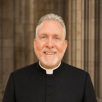 Smiling priest in traditional black clerical attire.