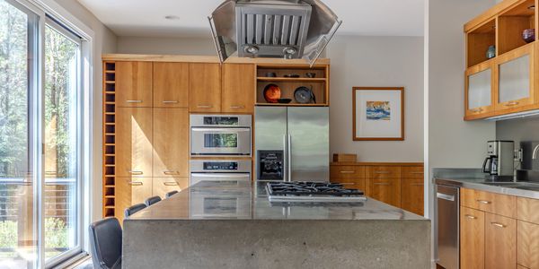 Modern kitchen with wooden cabinets, concrete island, and stainless steel appliances.