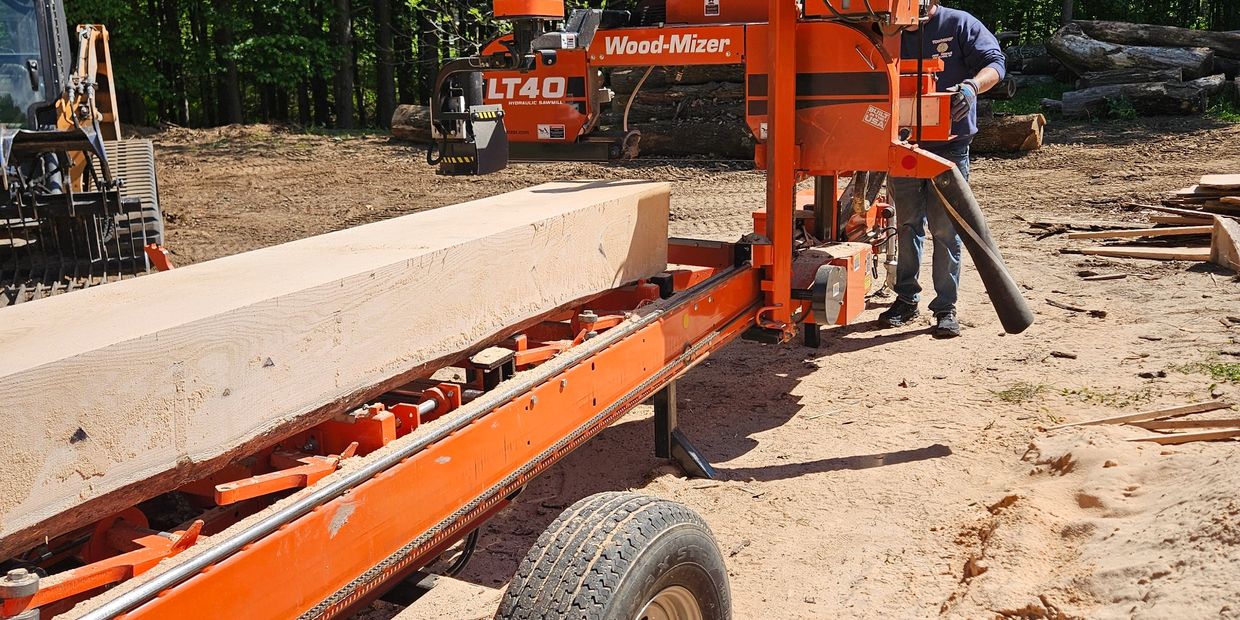 Orange Wood-Mizer sawmill cutting a large wooden beam outdoors.