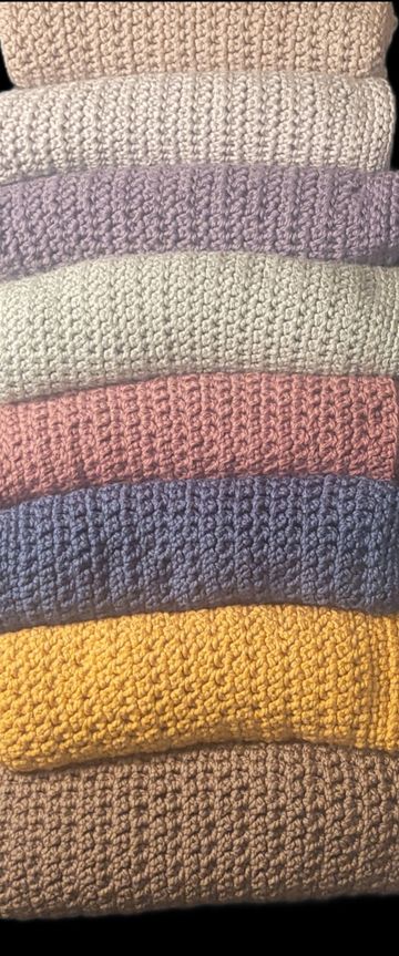 Stack of colorful crocheted blankets in various pastel and bright shades.