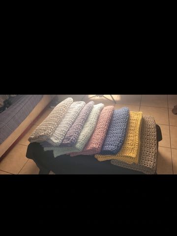 A row of colorful crocheted blankets neatly folded on a black surface.