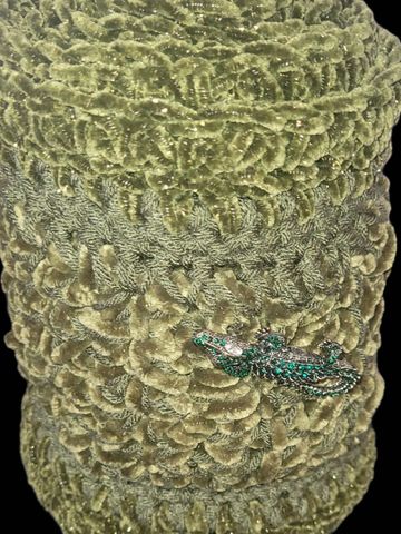 Intricately textured green fabric with a small decorative green alligator embellishment.