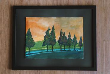 Framed watercolor painting of trees against an orange sky.