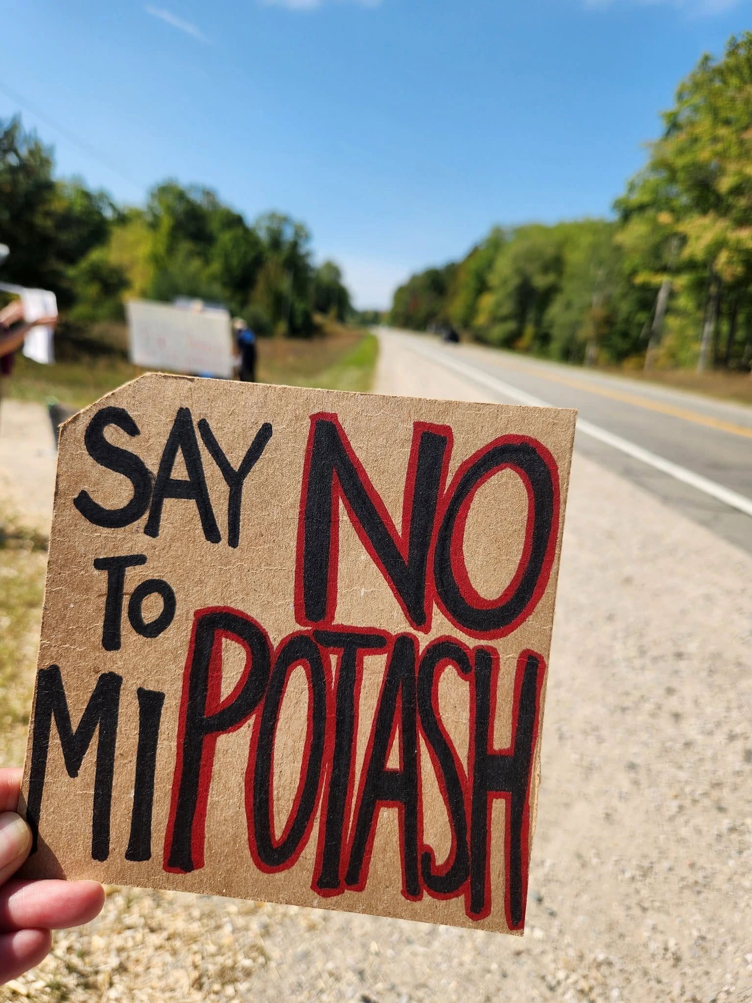 Close-up of a protest sign saying 'Say No to Mi Potash' held by a person near a road.
