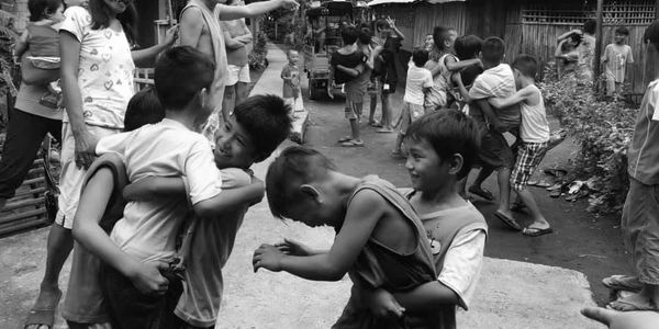 Children and adults happily playing and hugging in a rural village setting.