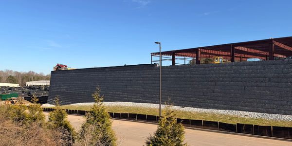 Large retaining wall with construction materials and a clear blue sky.