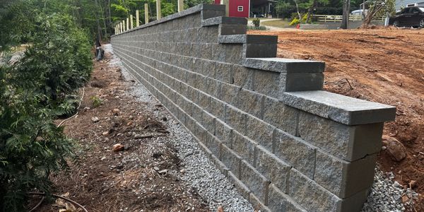 Newly built stepped retaining wall with gravel base near a construction site.