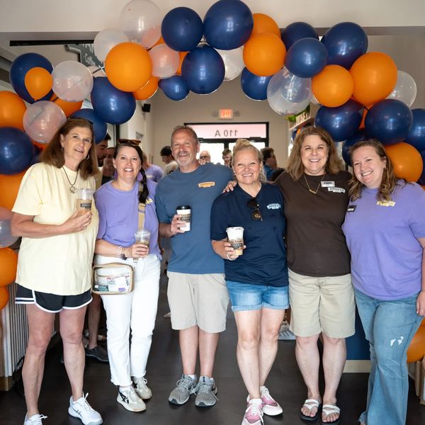 Group of six smiling friends under colorful balloons.
