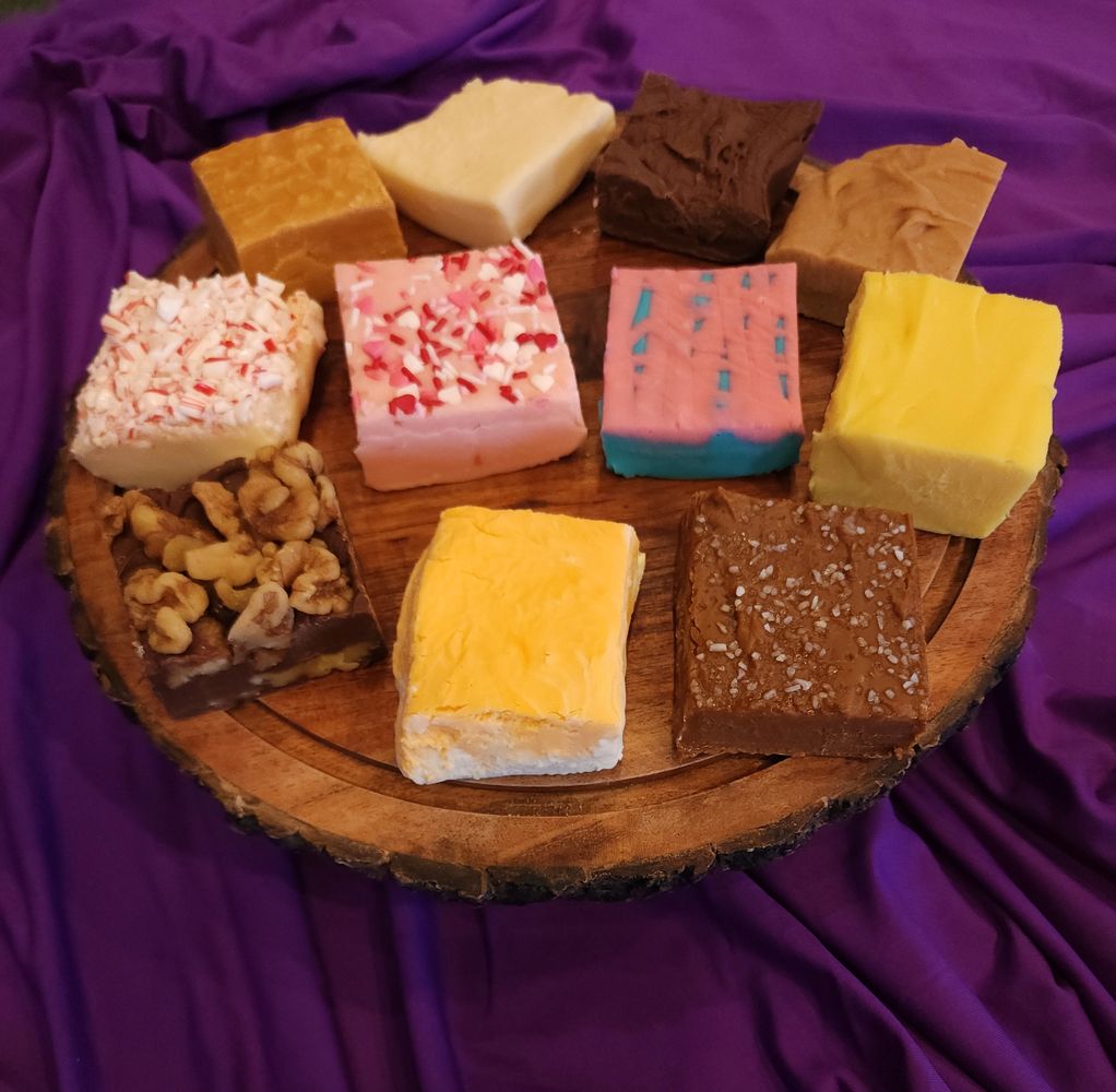 Assorted colorful fudge squares displayed on a wooden platter with a purple cloth background.
