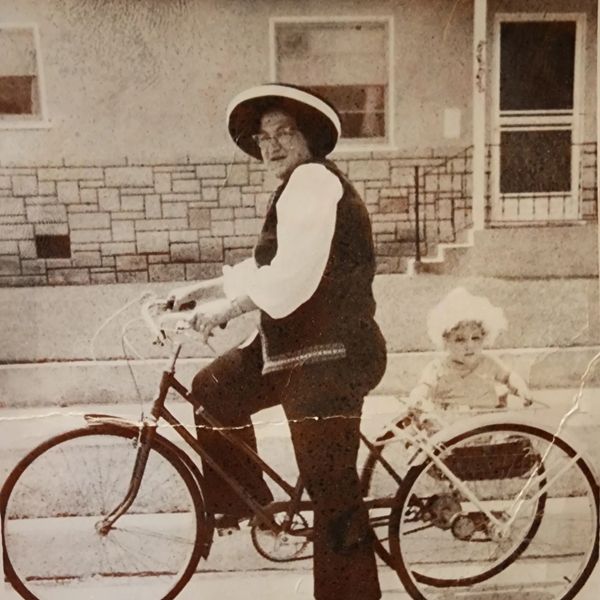 Vintage photo of a woman on a bicycle with a child seated in the back.