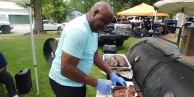 Man grilling meat outdoors with gloves.