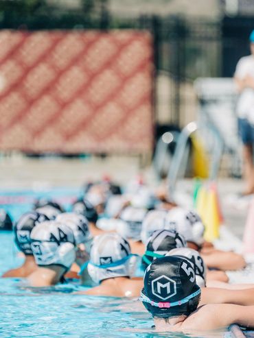 Young swimmers in caps lined up at pool edge.