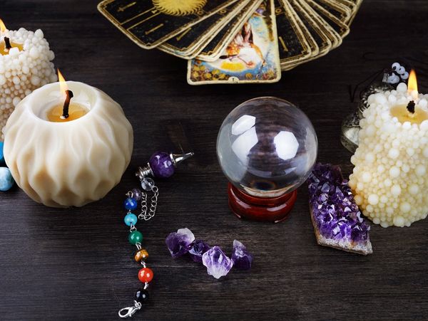 Crystal ball, amethyst stone, burning candles, a spread of tarot cards, and a chakra colored chain.