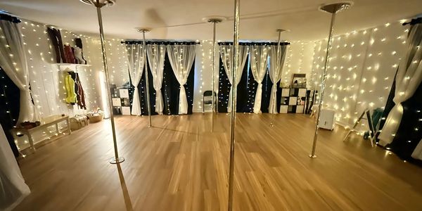 A cozy dance studio with poles and string lights.